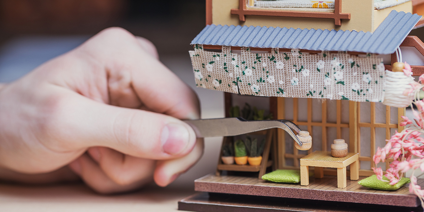 person placing wooden miniatures in a dollhouse